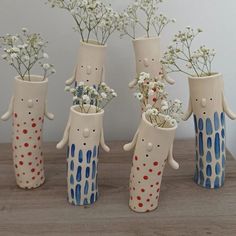 four ceramic vases with flowers in them sitting on a wooden table next to each other