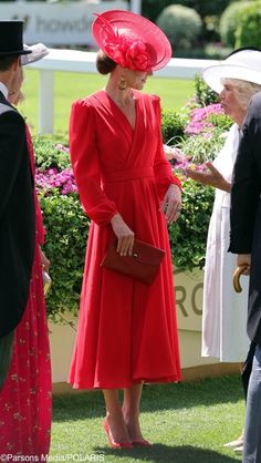 a woman in a red dress and hat standing next to other people on the grass