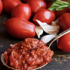 a spoon full of tomato sauce next to some tomatoes and garlic on a table with other vegetables