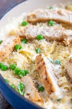 a blue bowl filled with pasta and meat covered in sauce, peas and parmesan cheese