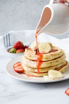 someone pouring syrup on some pancakes with bananas and strawberries