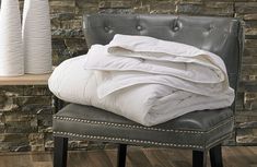 a white comforter sitting on top of a gray chair next to a brick wall