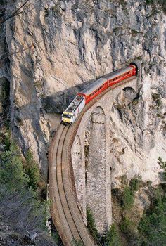 a train traveling over a bridge next to a mountain side covered in trees and rocks