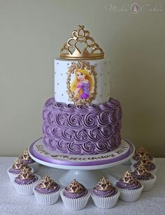 there is a purple and white cake with princesses on it, surrounded by cupcakes