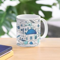 a coffee mug sitting on top of a wooden table next to a book and plant