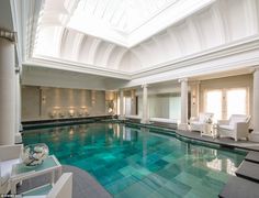 a large indoor swimming pool with blue water and white furniture in the center, surrounded by windows