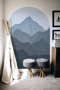 two stools sit in front of a wall with mountains painted on it and a teepee tent