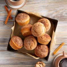 some sugared donuts are on a tray next to a cup of coffee and cinnamon sticks