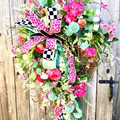 a wreath with pink flowers and green leaves hanging on a wooden fence next to a mailbox