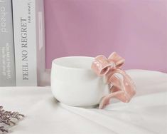 a white cup with a pink bow on the side sitting next to a bookcase