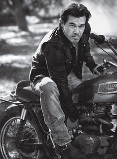 black and white photograph of a man sitting on a motorbike in the woods