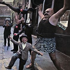 a group of people that are standing in the street with clown faces on their heads