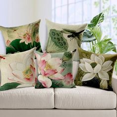 four pillows with flowers on them sitting on a couch next to a potted plant