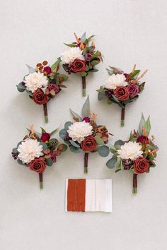 wedding bouquets with flowers and foliage arranged on the wall next to an orange piece of paper