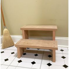 two wooden step stools sitting on top of a white tiled floor next to a broom