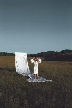 a person standing in a field with a white cloth covering their face and arms over his head