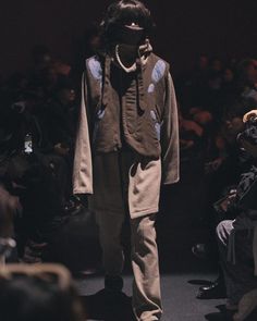 a man walking down a runway in front of a group of people wearing face coverings