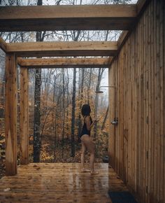 a woman in a black bathing suit standing on a wooden platform next to a forest