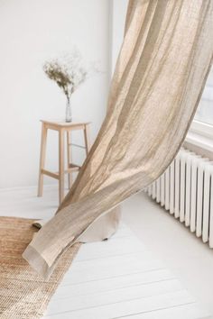 a white radiator sitting next to a window covered in sheer curtains and a vase with flowers