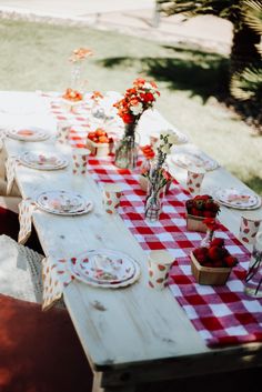 an outdoor table set with plates and flowers