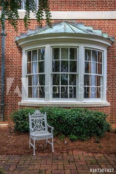 a white bench sitting in front of a brick building next to a tree and bushes