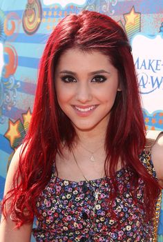 a woman with long red hair smiling at the camera and wearing a flowery top