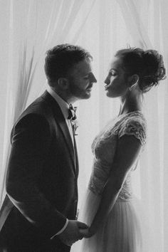 a man and woman standing next to each other in front of a window with curtains