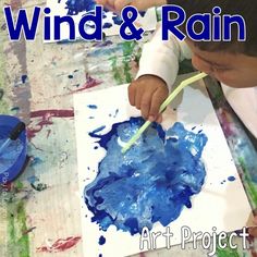 a young boy painting with blue paint on paper and the words wind & rain above it