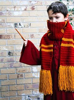 a young boy dressed in red and yellow holding a stick while standing next to a brick wall