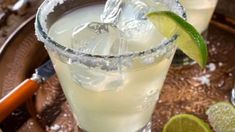 two glasses filled with ice and limes on top of a table next to silverware