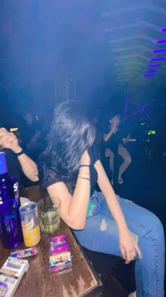 a woman sitting at a table in front of a blue bottle and some liquor bottles