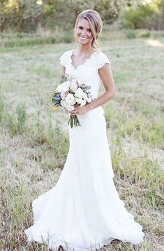 a woman in a white dress holding a bouquet of flowers and smiling at the camera