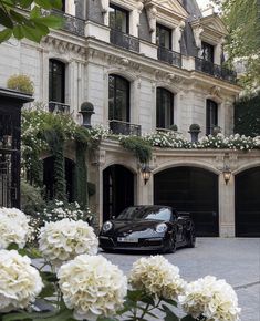 a black sports car parked in front of a building with white flowers on the driveway