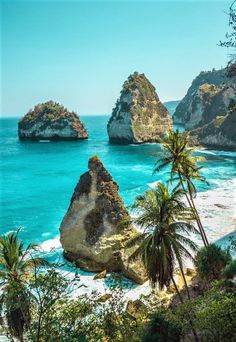 an ocean view with rocks and palm trees on the shore, surrounded by blue water