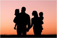 the silhouette of two adults and a child at sunset