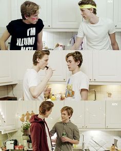 two young men standing next to each other in a kitchen and one is eating food