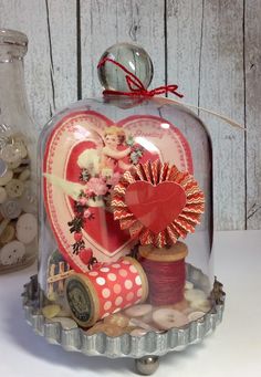 a glass cloche with buttons and thread in it next to a vase filled with hearts