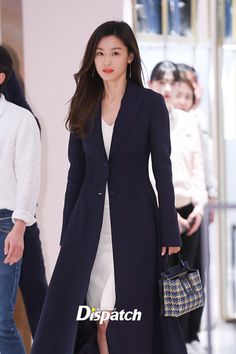 a woman walking down a runway carrying a purse and wearing a long black coat over her shoulders