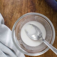 a glass bowl filled with yogurt next to a spoon on top of a wooden table