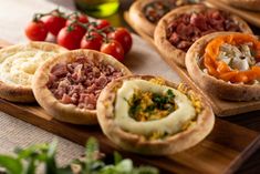 several different types of food are displayed on a cutting board next to tomatoes and other vegetables