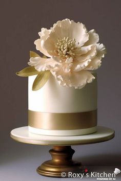 a white and gold wedding cake with large flowers on the top, sitting on a pedestal