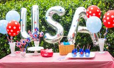 a table with balloons and decorations for a fourth of july party in front of bushes