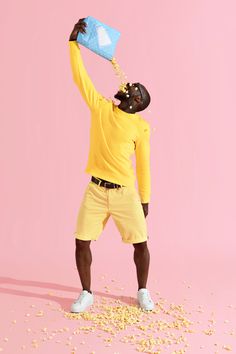 a man standing in front of a pink background drinking from a blue cup with sprinkles on it