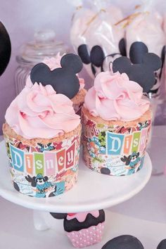 two cupcakes with pink frosting and minnie mouse ears on top are sitting on a cake plate