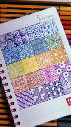 an open notebook with colorful designs on the pages and colored pencils next to it