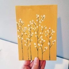 a hand holding up a piece of yellow paper with white flowers painted on the side