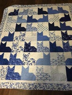 a blue and white quilt with cats on it's sides, sitting on a wooden floor