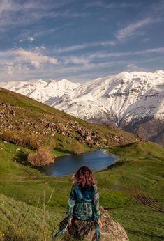 a woman sitting on top of a rock in front of a lake and snow covered mountains