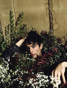 a man laying in the middle of flowers with his hand on his head and looking at the camera