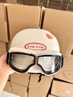 a person holding up a white helmet with goggles on it's face in front of boxes